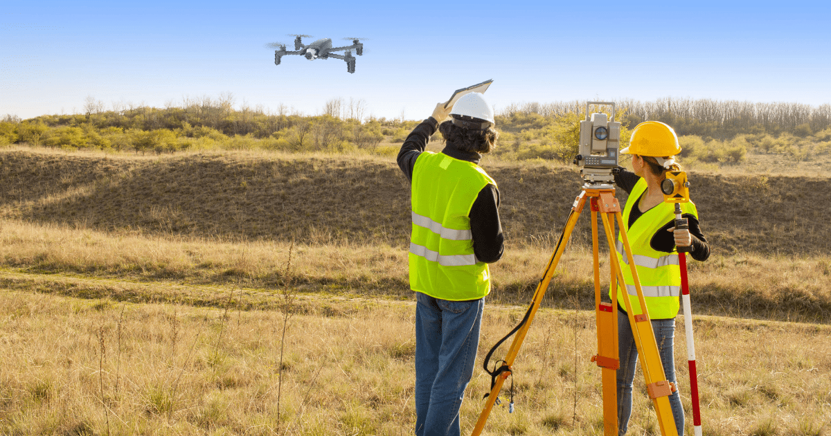 Equipo topográfico con estación en tierra mientras un dron sobrevuela la zona de trabajo