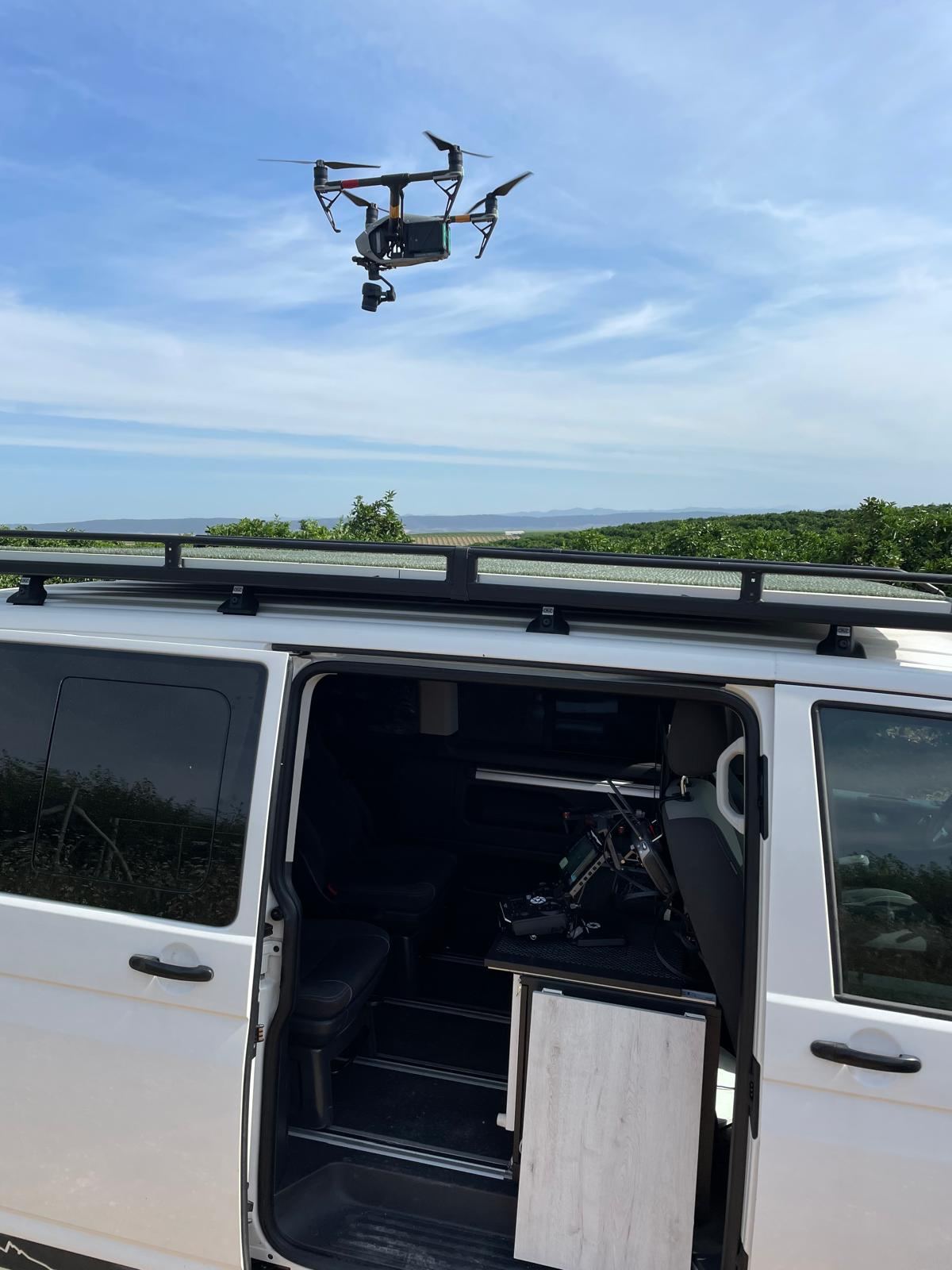 Furgoneta del equipo cargada y con el dron en vuelo antes de una cobertura